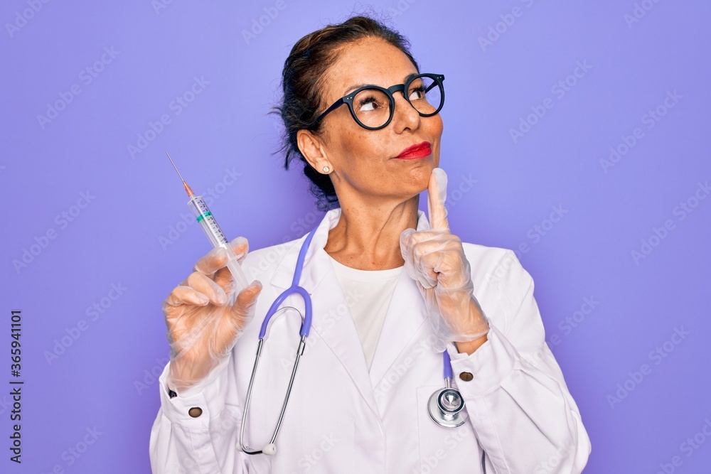 Middle age senior professional doctor woman holding syringe with medical vaccine serious face thinking about question, very confused idea Middle age senior professional doctor woman holding syringe with medical vaccine serious face thinking about question, very confused idea