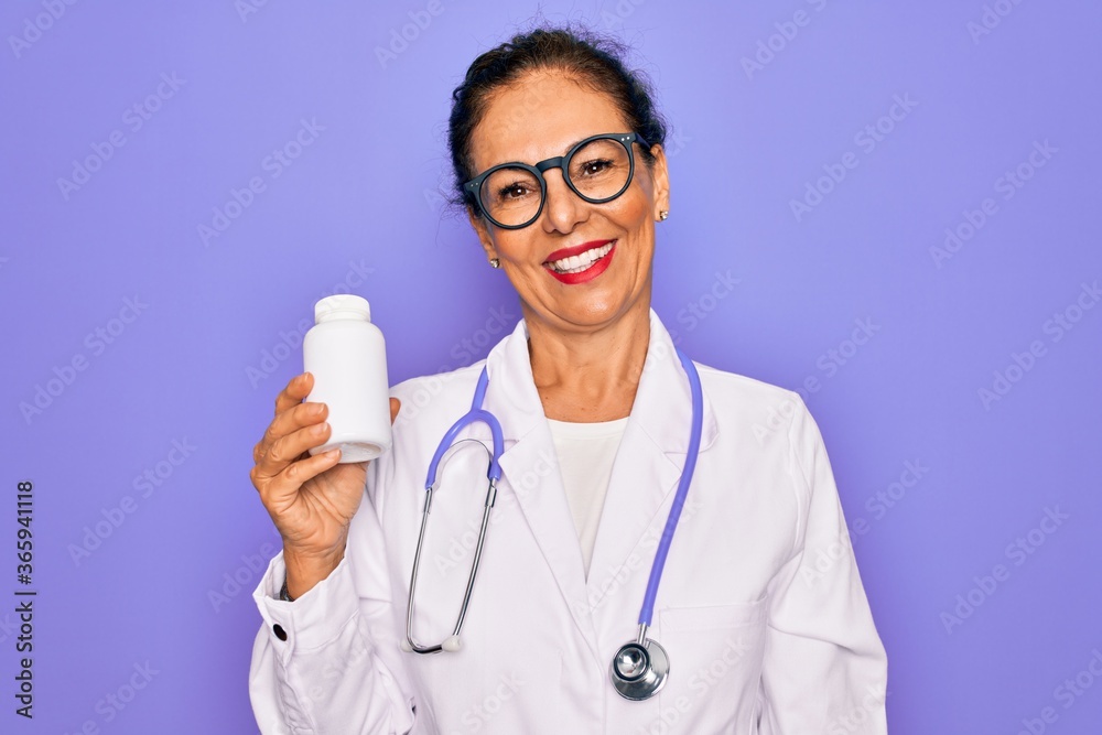 Middle age senior professional doctor woman holding pharmaceutical pills with a happy face standing and smiling with a confident smile showing teeth Middle age senior professional doctor woman holding pharmaceutical pills with a happy face standing and smiling with a confident smile showing teeth