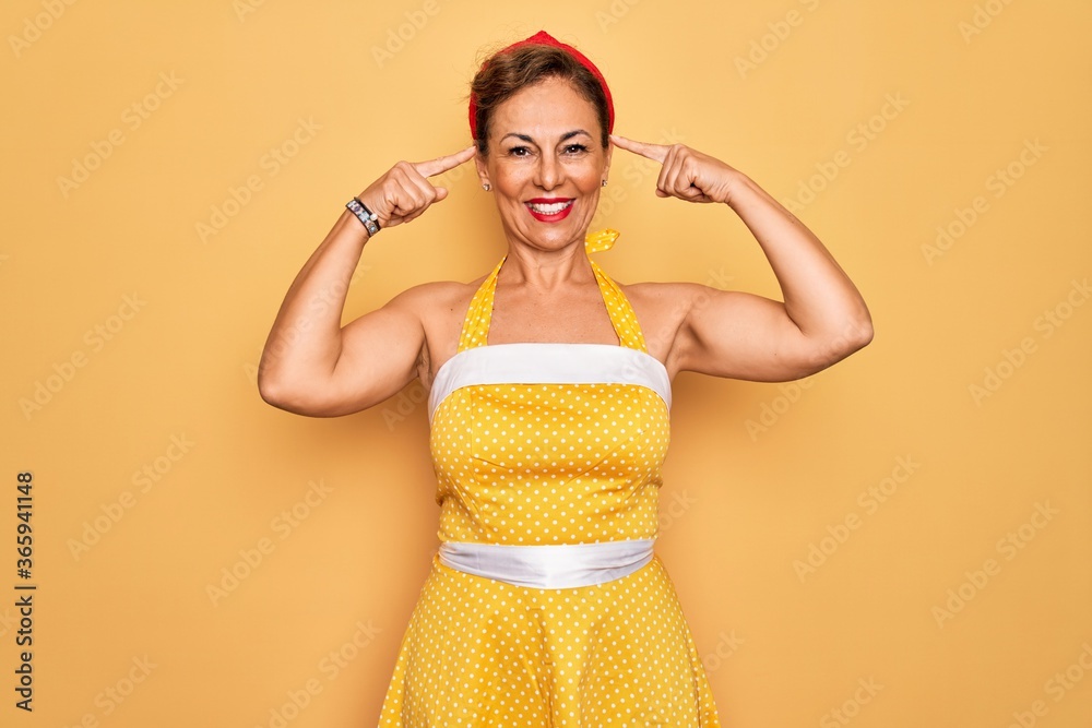 Middle age senior pin up woman wearing 50s style retro dress over yellow  background smiling pointing to head with both hands finger, great idea or  thought, good memory Stock Photo