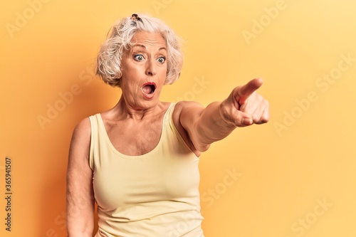 Senior grey-haired woman wearing casual clothes pointing with finger surprised ahead, open mouth amazed expression, something on the front photo