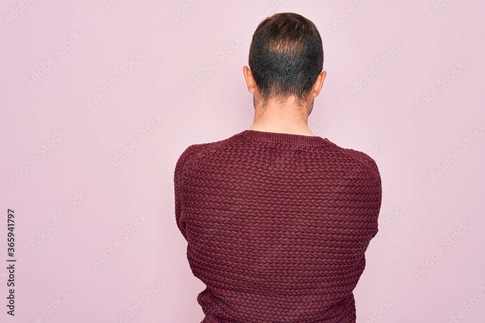 Young handsome man with blue eyes wearing casual sweater standing over pink background standing backwards looking away with crossed arms Young handsome man with blue eyes wearing casual sweater standing over pink background standing backwards looking away with crossed arms