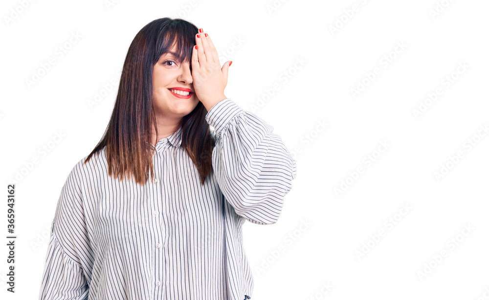 Young plus size woman wearing casual clothes covering one eye with hand, confident smile on face and surprise emotion. Young plus size woman wearing casual clothes covering one eye with hand, confident smile on face and surprise emotion.
