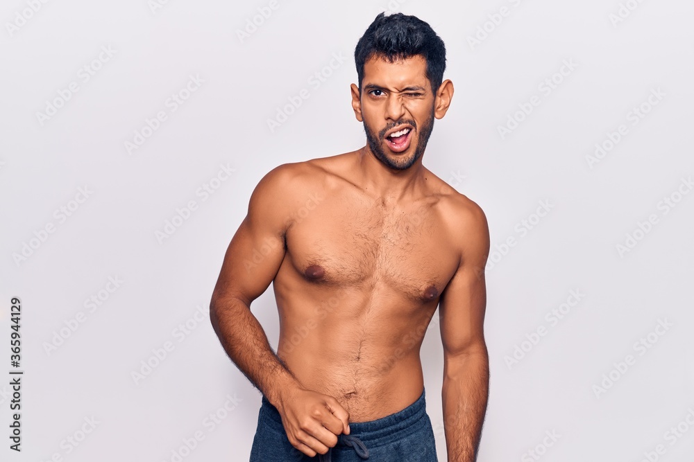 Young latin man standing shirtless winking looking at the camera with sexy expression, cheerful and happy face.