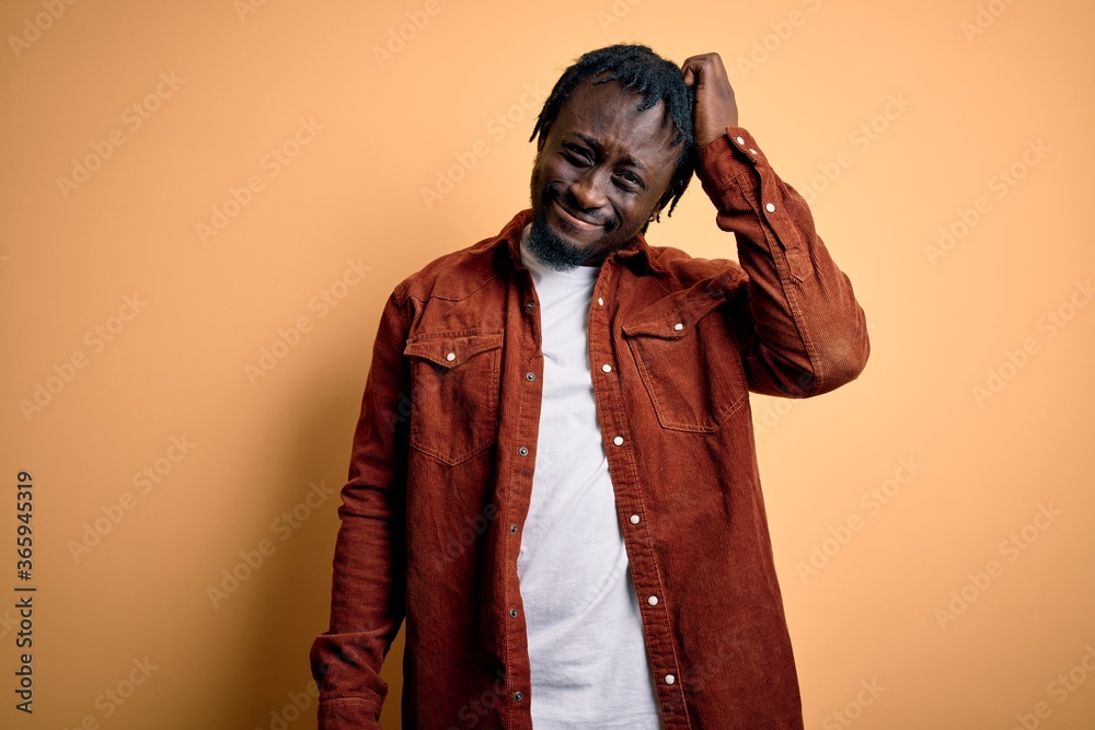 Young handsome african american man wearing casual jacket standing over yellow background confuse and wonder about question. Uncertain with doubt, thinking with hand on head. Pensive concept. Young handsome african american man wearing casual jacket standing over yellow background confuse and wonder about question. Uncertain with doubt, thinking with hand on head. Pensive concept.