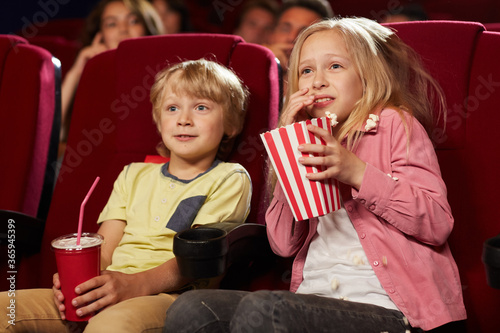 Tablou pe pânză Portrait of two cute scared kids watching movie in cinema theater and eating pop