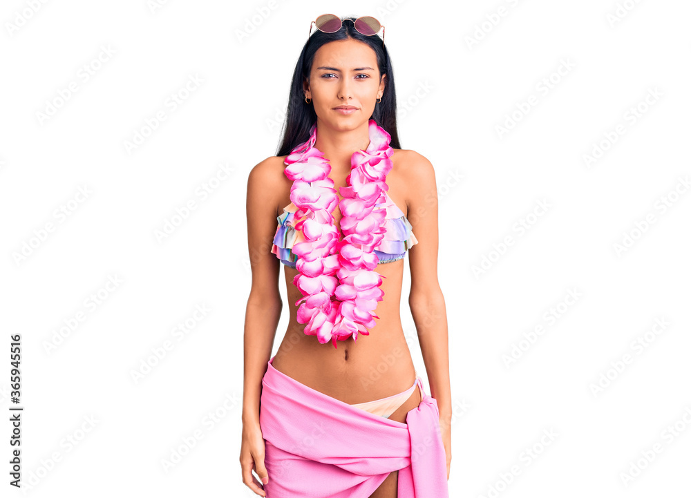 Young beautiful latin girl wearing bikini and hawaiian lei with serious expression on face. simple and natural looking at the camera. Young beautiful latin girl wearing bikini and hawaiian lei with serious expression on face. simple and natural looking at the camera.