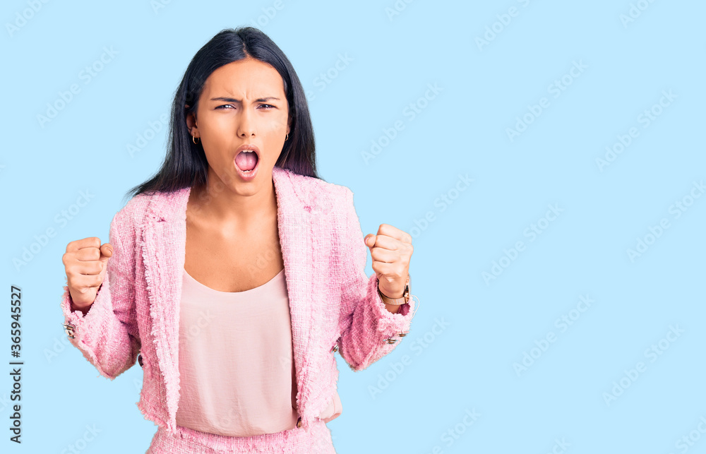 Young beautiful latin girl wearing business clothes angry and mad raising fists frustrated and furious while shouting with anger. rage and aggressive concept.