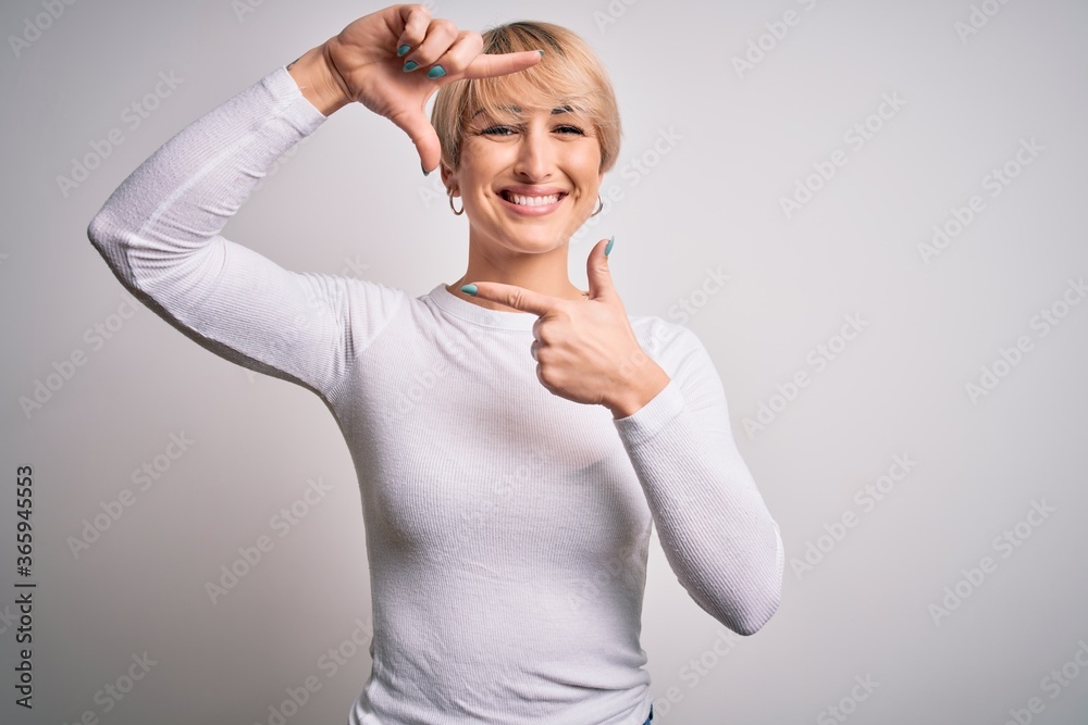 Fototapeta premium Young beautiful blonde woman with modern short hair hairstyle standing over isolated background smiling making frame with hands and fingers with happy face. Creativity and photography concept.