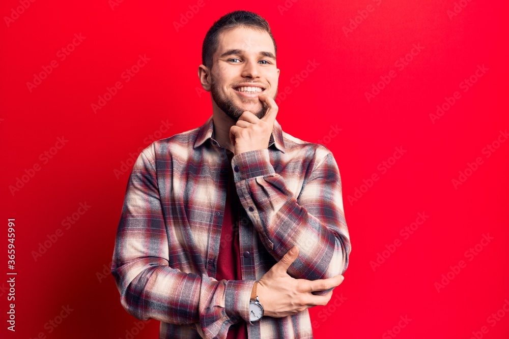 Young handsome man wearing casual shirt smiling looking confident at the camera with crossed arms and hand on chin. thinking positive.