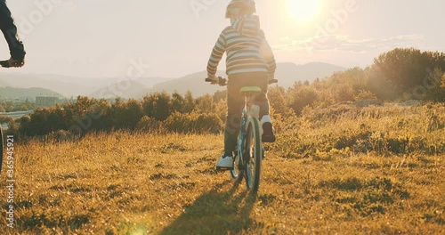 Father and son ride a bike. Happy cute boy in helmet learn to riding a bike in park on green meadow in summer day at sunset time. Family weekend. 4K video, Slow motion