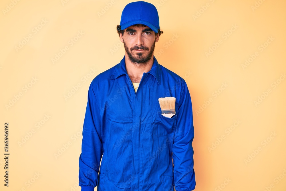 Handsome young man with curly hair and bear wearing builder jumpsuit uniform skeptic and nervous, frowning upset because of problem. negative person.