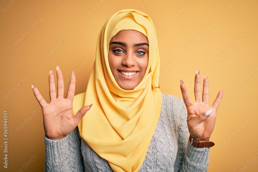Young beautiful african american girl wearing muslim hijab over isolated yellow background showing and pointing up with fingers number nine while smiling confident and happy. Young beautiful african american girl wearing muslim hijab over isolated yellow background showing and pointing up with fingers number nine while smiling confident and happy.