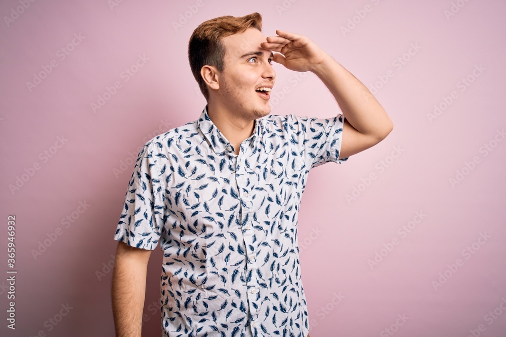 Young handsome redhead man wearing casual summer shirt standing over pink background very happy and smiling looking far away with hand over head. Searching concept. Young handsome redhead man wearing casual summer shirt standing over pink background very happy and smiling looking far away with hand over head. Searching concept.