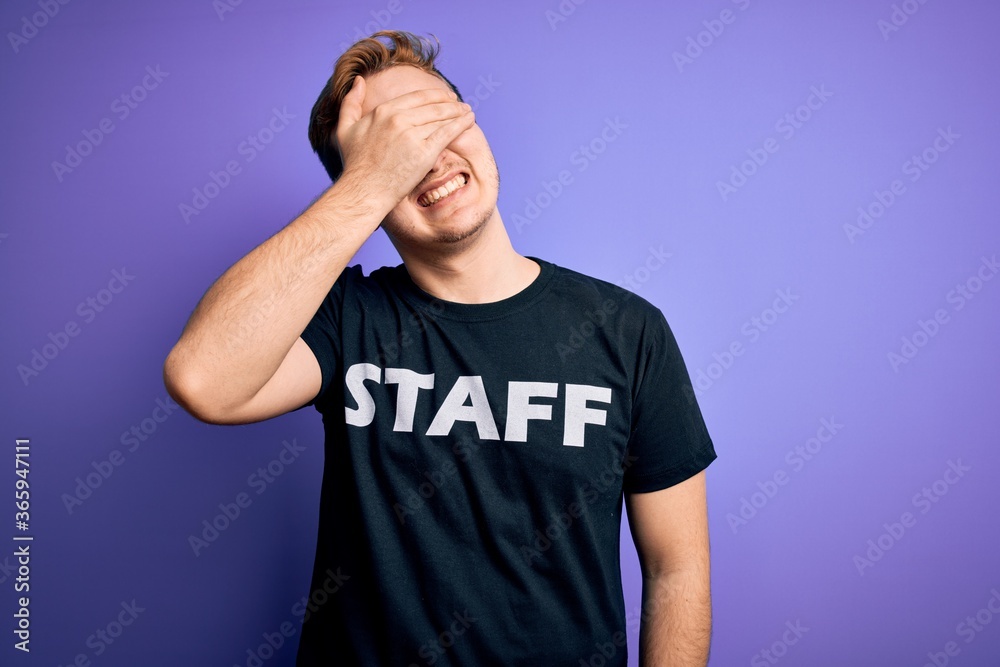 Young handsome redhead worker man wearing staff t-shirt uniform over purple background smiling and laughing with hand on face covering eyes for surprise. Blind concept. Young handsome redhead worker man wearing staff t-shirt uniform over purple background smiling and laughing with hand on face covering eyes for surprise. Blind concept.