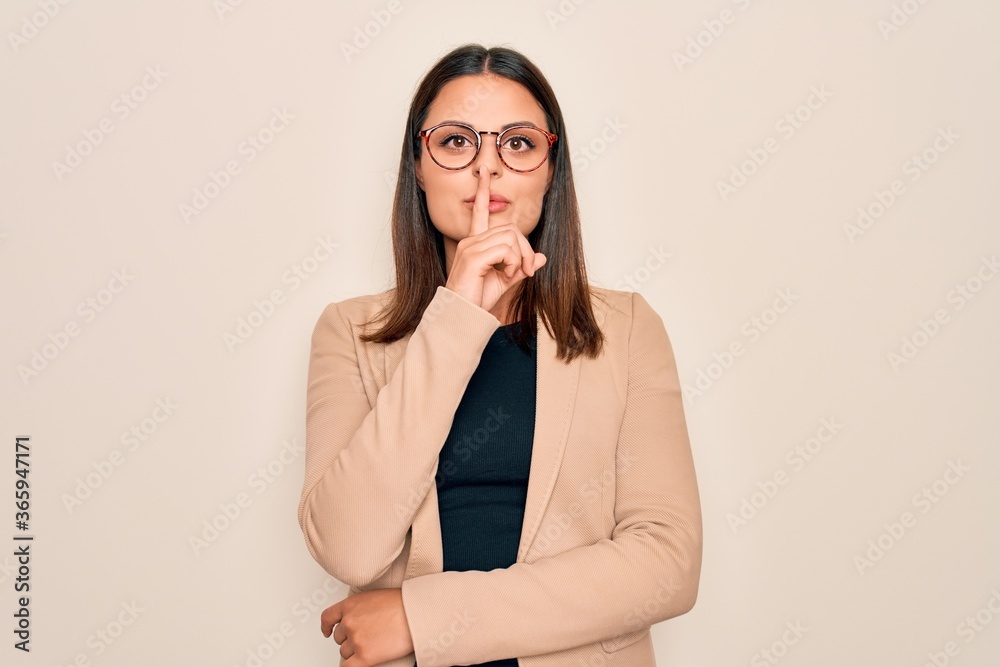 Young beautiful brunette businesswoman wearing jacket and glasses over white background asking to be quiet with finger on lips. Silence and secret concept. Young beautiful brunette businesswoman wearing jacket and glasses over white background asking to be quiet with finger on lips. Silence and secret concept.
