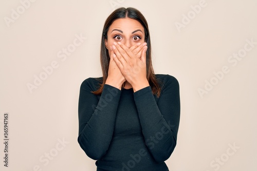 Young beautiful brunette woman wearing casual t-shirt standing over isolated white background shocked covering mouth with hands for mistake. Secret concept.
