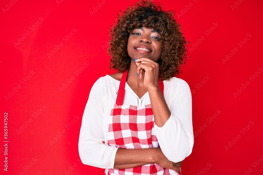 Young african american woman wearing apron smiling looking confident at the camera with crossed arms and hand on chin. thinking positive. Young african american woman wearing apron smiling looking confident at the camera with crossed arms and hand on chin. thinking positive.