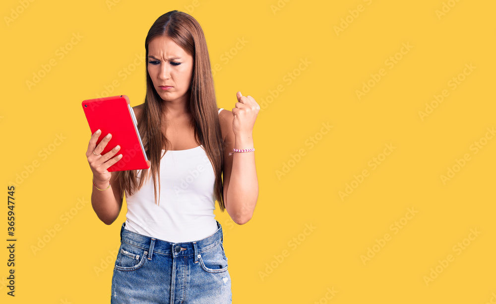 Young beautiful hispanic woman holding touchpad annoyed and frustrated shouting with anger, yelling crazy with anger and hand raised Young beautiful hispanic woman holding touchpad annoyed and frustrated shouting with anger, yelling crazy with anger and hand raised