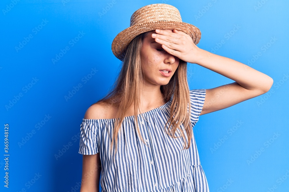 Young beautiful girl wearing summer hat and striped t-shirt surprised with hand on head for mistake, remember error. forgot, bad memory concept.