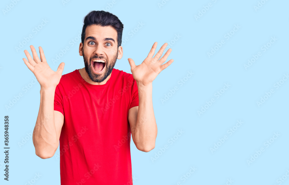 Young handsome man with beard wearing casual t-shirt celebrating crazy and amazed for success with arms raised and open eyes screaming excited. winner concept Young handsome man with beard wearing casual t-shirt celebrating crazy and amazed for success with arms raised and open eyes screaming excited. winner concept