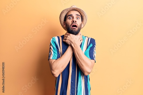 Young handsome man with beard wearing summer hat and shirt shouting and suffocate because painful strangle. health problem. asphyxiate and suicide concept.