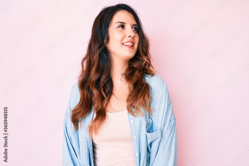 Young beautiful brunette woman wearing casual clothes over pink background looking away to side with smile on face, natural expression. laughing confident. Young beautiful brunette woman wearing casual clothes over pink background looking away to side with smile on face, natural expression. laughing confident.