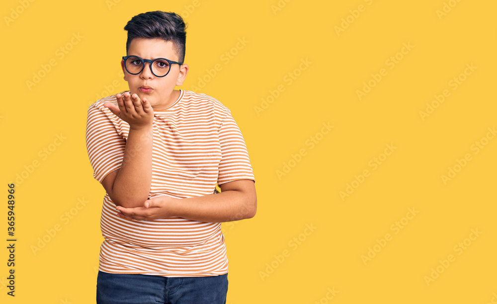 Little boy kid wearing casual clothes and glasses looking at the camera blowing a kiss with hand on air being lovely and sexy. love expression. Little boy kid wearing casual clothes and glasses looking at the camera blowing a kiss with hand on air being lovely and sexy. love expression.