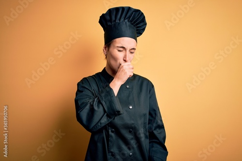 Young beautiful chef woman wearing cooker uniform and hat standing over yellow background feeling unwell and coughing as symptom for cold or bronchitis. Health care concept.