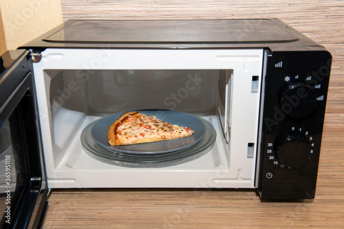 Plate with slice of pizza in microwave oven