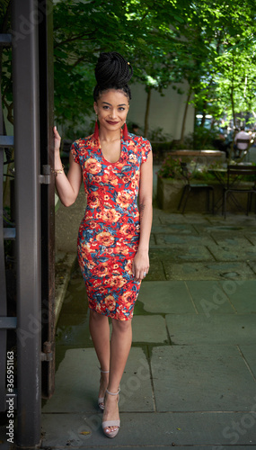 Stunning young biracial woman stands outside wearing standing at gate to small city park