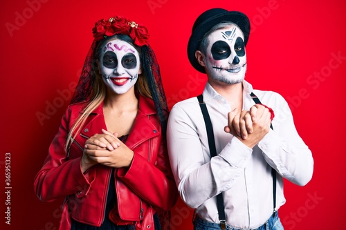 Couple wearing day of the dead costume over red with hands together and crossed fingers smiling relaxed and cheerful. success and optimistic