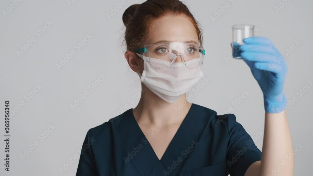 Professional female doctor in protective eyeglasses, mask and medical gloves working with flask isolated