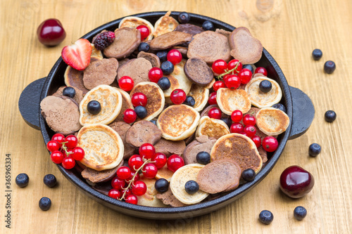 Pancake and berries in pan. Light wood background.