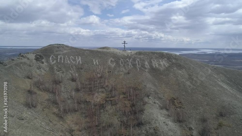 Orthodox cross on Mount Karabash. The camera flies away from them in the distance. The Title on the mountain: “Bless and save”. Russia, Chelyabinsk region
