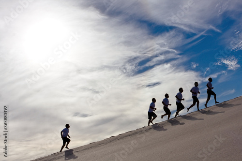 Fotografia business concept success,competition,people running uphill outdoors su clouds an