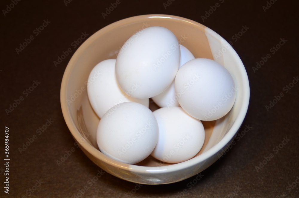 white chicken eggs in a two-color bowl located on a dark background white chicken eggs in a two-color bowl located on a dark background