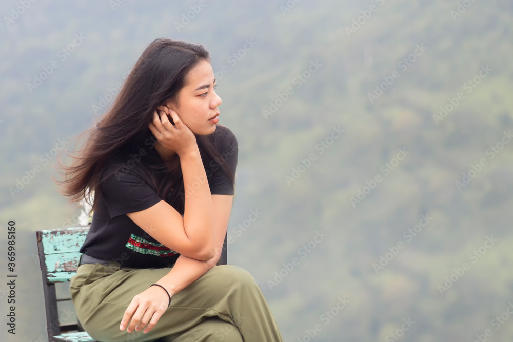 Asian woman is sitting on a wooden table waiting to watch the sunrise in the morning at rural , Thailand. Beautiful girl sitting on wooden chair with blurred green background.