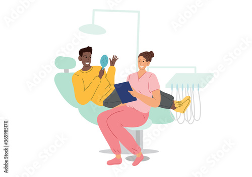 The patient sits in a dental chair and looks in the mirror at his teeth, at his white smile. At the dentists appointment.