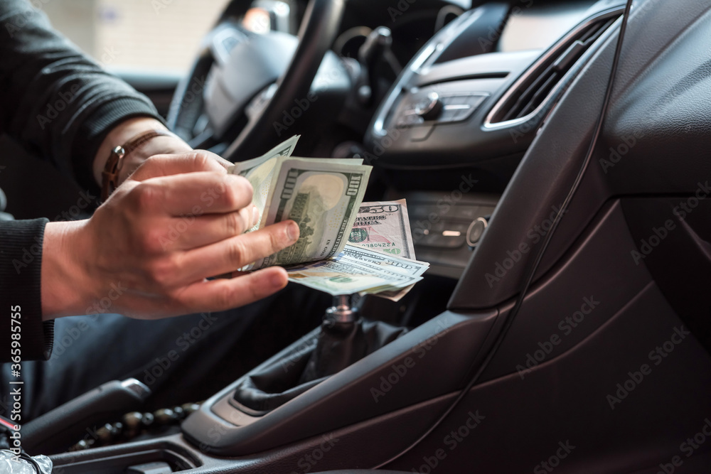 Man  sitting in a car counting dollar banknotes for or as bribes, insurance or credit, investing