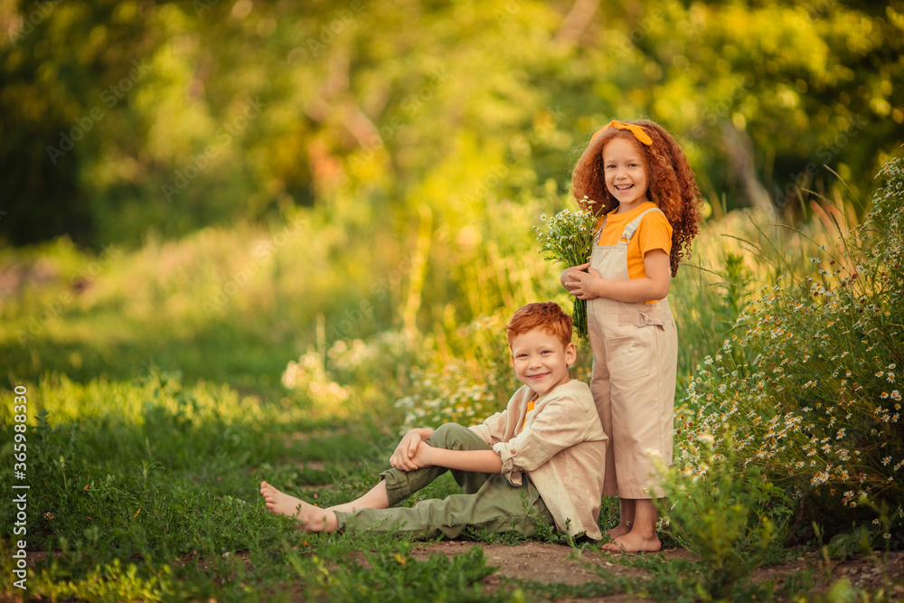 Fototapeta premium Cheerful happy Children brother and sister on a walk in the forest with a bouquet of daisies.