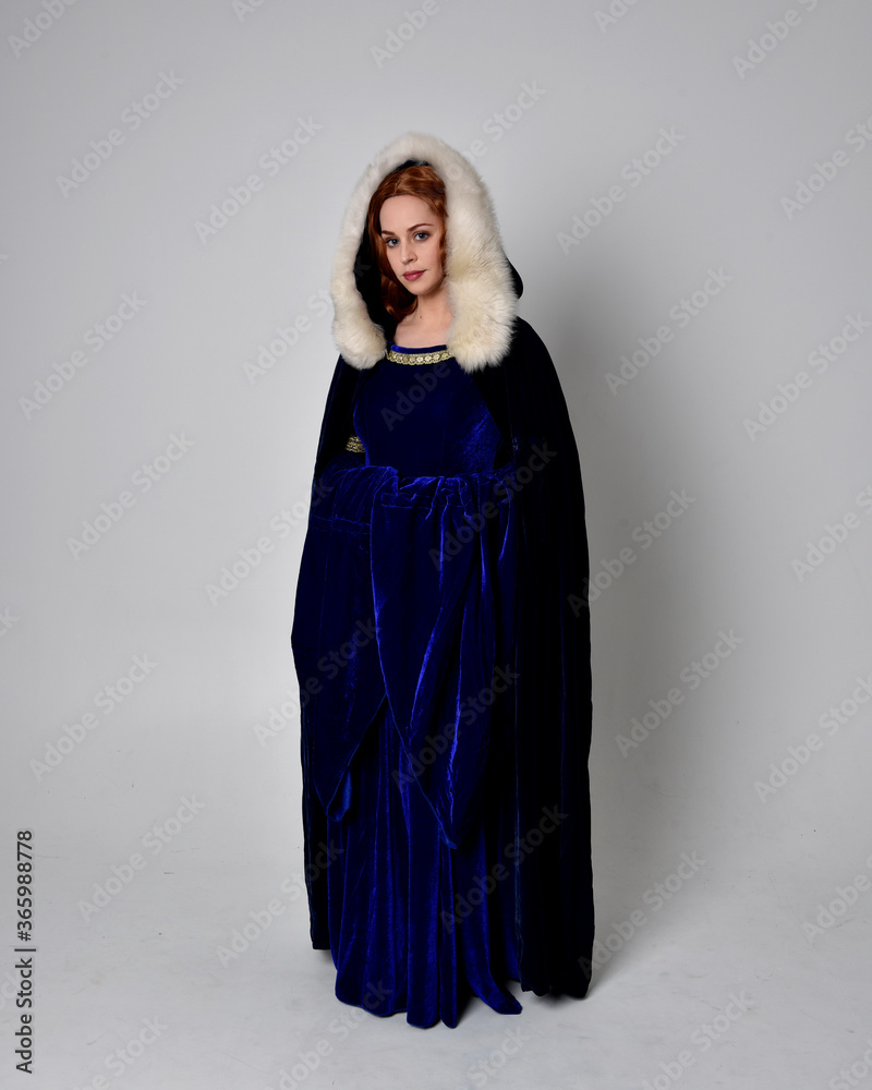 Full length portrait of girl wearing long blue velvet gown with golden crown. sitting pose, isolated against a studio background. Full length portrait of girl wearing long blue velvet gown with golden crown. sitting pose, isolated against a studio background.