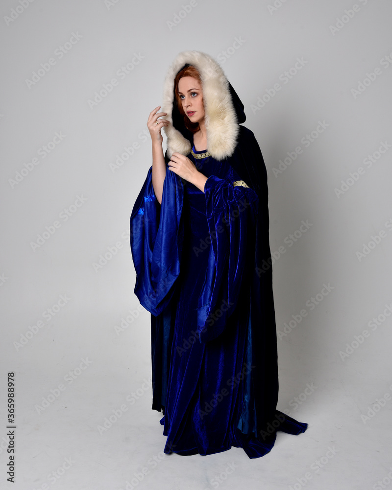 Full length portrait of girl wearing long blue velvet gown with golden crown. sitting pose, isolated against a studio background. Full length portrait of girl wearing long blue velvet gown with golden crown. sitting pose, isolated against a studio background.