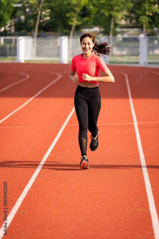 A young fitness woman runner jogging excercise in the morning on city stadium track in the city. Female athlete excercise in the city stadium to keep body fitness. Health and recreation stock photo.