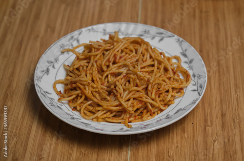 Tomato and tomato paste spaghetti on white plate on wooden patterned table