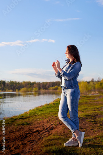 Girl or woman standing on the shore or beach of the lake in the evening at sunset.