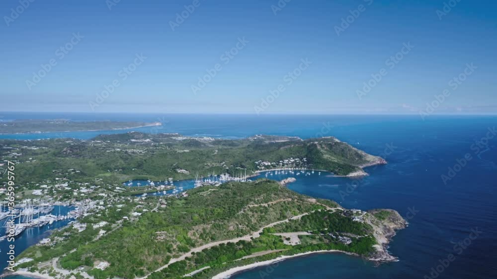Drone shoots a hilly island with dense vegetation and marina with white yachts from a bird's eye view (Antigua and Barbuda) Drone shoots a hilly island with dense vegetation and marina with white yachts from a bird's eye view (Antigua and Barbuda)