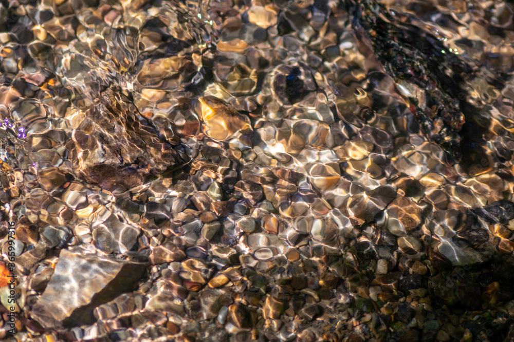 Silky ripples in water of a crystal clear water creek as idyllic natural background with high angle view shows zen meditation and little waves in a healthy mountain spring with a clear floating stream Silky ripples in water of a crystal clear water creek as idyllic natural background with high angle view shows zen meditation and little waves in a healthy mountain spring with a clear floating stream