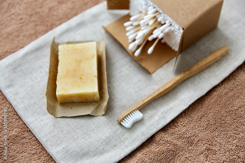 natural cosmetics, sustainability and eco living concept - wooden toothbrush, handmade soap cotton swabs on canvas