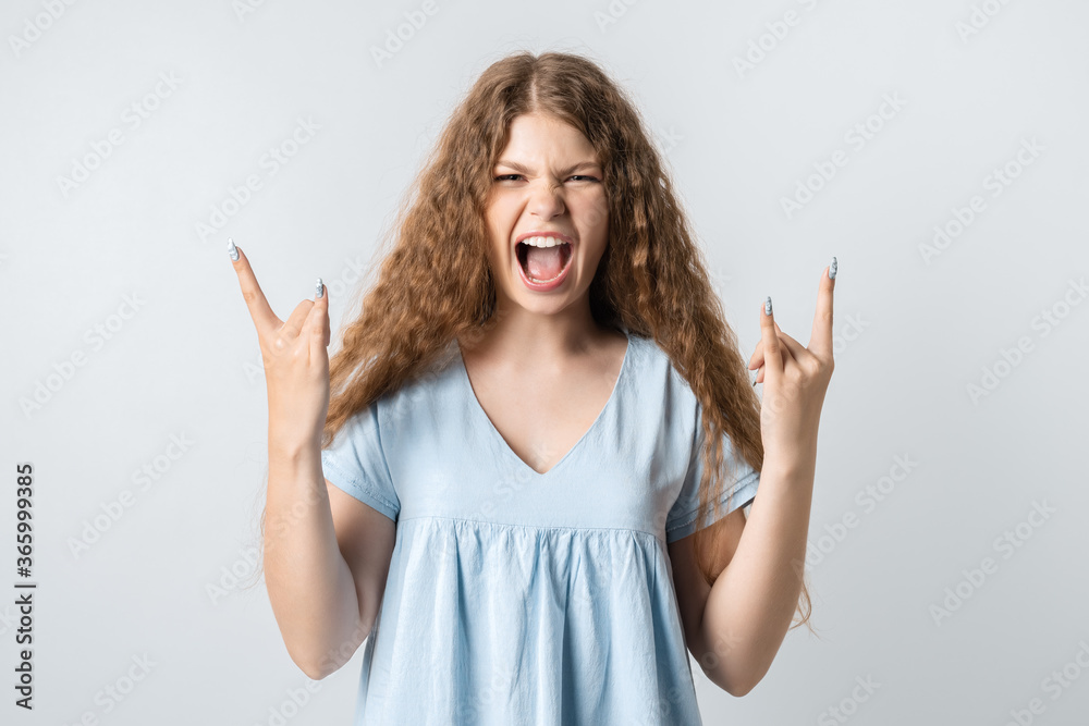 Emotive European young woman with curly long hair makes ROCK-N-ROLL sign, says: I will rock this party! yells loudly, wears casual t-shirt, stands over white background, feels self confident Emotive European young woman with curly long hair makes ROCK-N-ROLL sign, says: I will rock this party! yells loudly, wears casual t-shirt, stands over white background, feels self confident