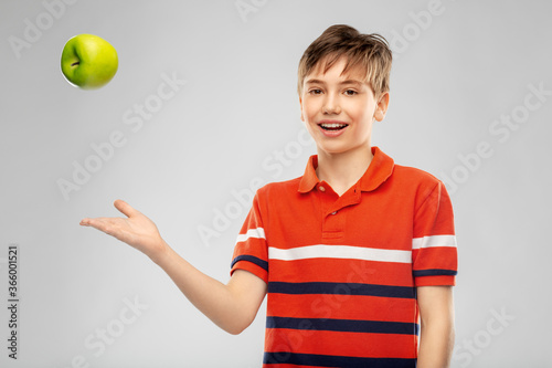 food, healthy eating and people concept - portrait of happy smiling boy in red polo t-shirt throwing green apple over grey background